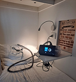 A C-PAP machine sitting on a fold-out ledge above a bed in a hostel.