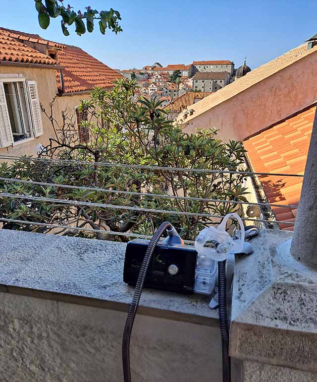 A C-PAP machine sitting on a wide porch railing overlooking terracotta tiled roofs in a Croatian city.